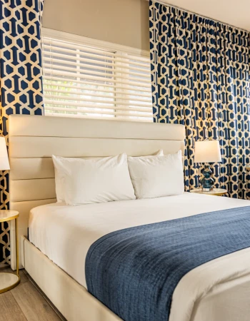 A stylish bedroom with a bed, blue geometric curtains, a desk, two lamps, and a chair, creating a cozy and modern atmosphere.