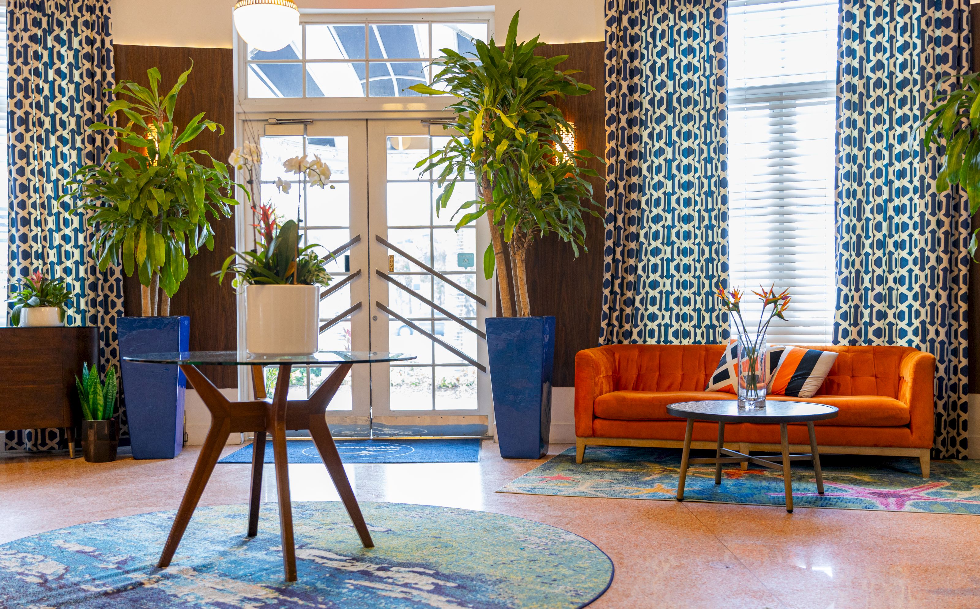 A bright and colorful lobby with a glass table, orange sofa, and potted plants.