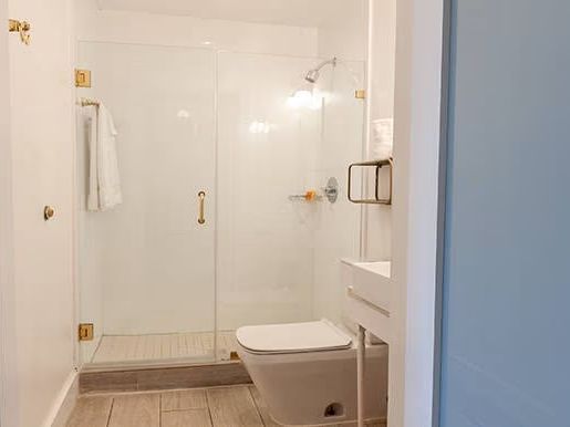 A modern bathroom with a glass shower enclosure, a towel on the rack, and a wall-mounted toilet against white walls and wooden flooring.
