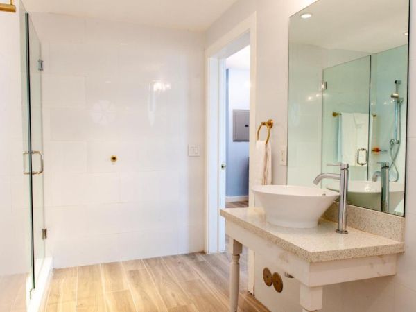 The image shows a modern bathroom with a glass shower, vessel sink, large mirror, and towel hanging on a golden ring holder.