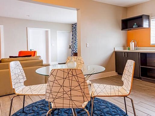 A modern living space with a seating area, glass table, decorative chairs, and a kitchenette with countertop.