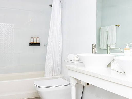 A bright bathroom featuring a bathtub, shower curtain, toilet, and sink with soaps and towels on a white counter.