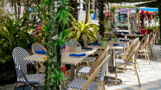 An outdoor dining area with tables and chairs surrounded by plants
