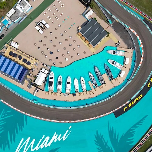 Aerial view of a race track with yachts docked nearby, surrounded by teal blue areas, marked "Miami" and "P Zero" on the track.