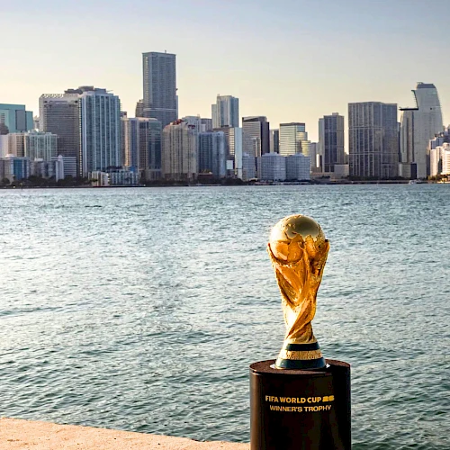 A trophy sits on a quay by the water with a city skyline in the background across the bay, gleaming in the sunset.