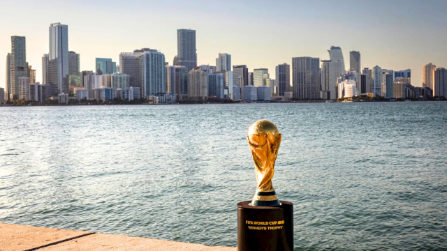 A trophy sits on a quay by the water with a city skyline in the background across the bay, gleaming in the sunset.