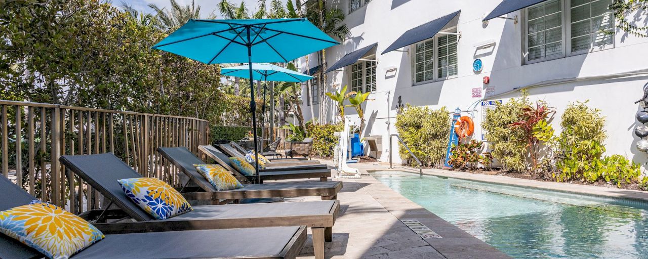 A poolside scene with lounge chairs, umbrellas, and a building in the background.