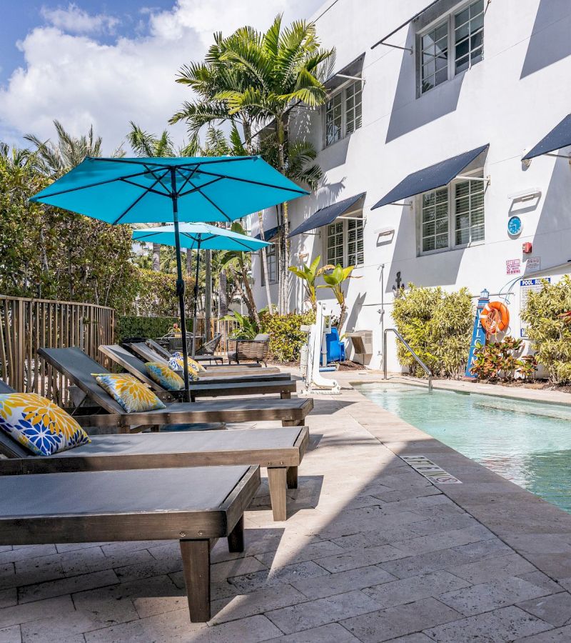 A poolside scene with lounge chairs, umbrellas, and a building in the background.