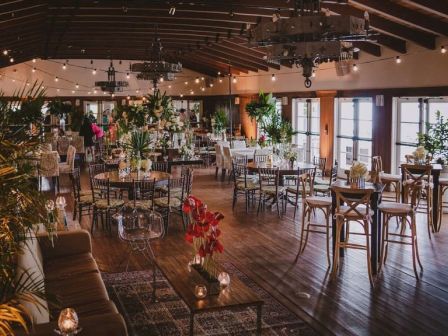 A spacious, stylish restaurant with wooden floors, modern lighting, and a mix of high tables and chairs, lush plants, and intimate candlelit corners.