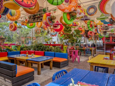 A colorful outdoor dining area with bright seating and tables, plus playful inflatable decorations hanging above. (End of sentence.)