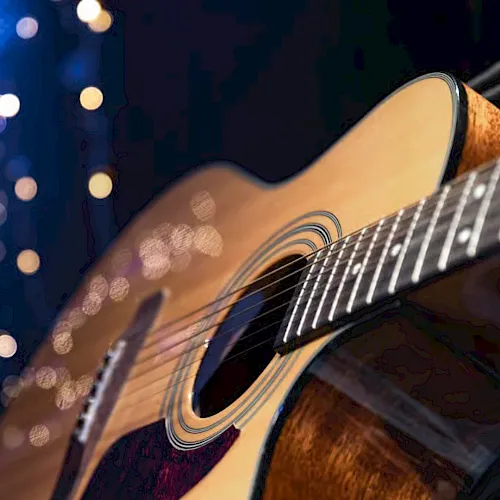 Close-up of an acoustic guitar&rsquo;s soundboard and strings, glowing under blue night lights and bokeh.
