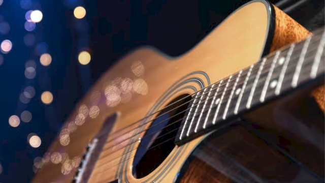 Close-up of an acoustic guitar&rsquo;s soundboard and strings, glowing under blue night lights and bokeh.